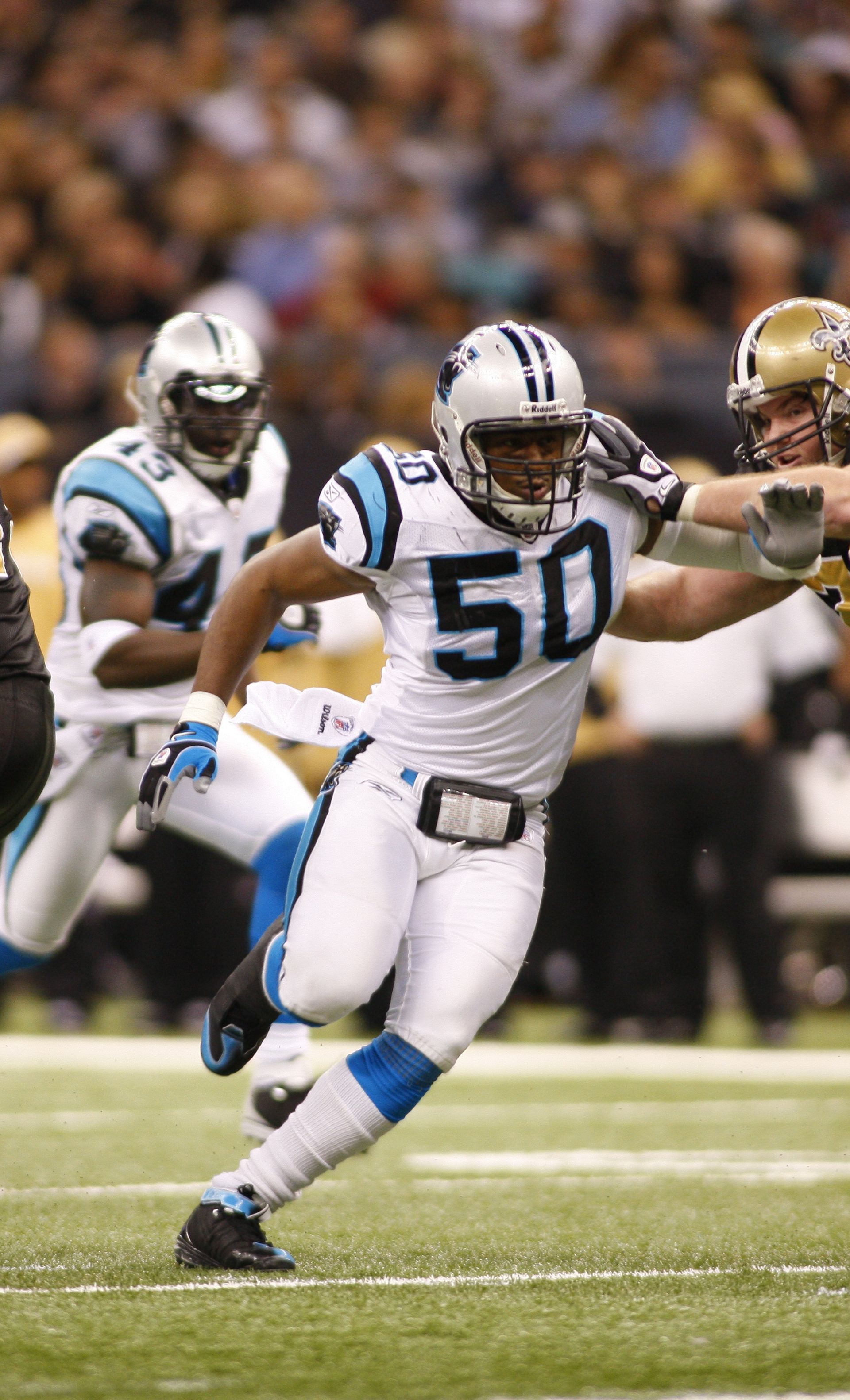 Football player in a Carolina Panthers uniform (#50) running on a field, opponent in the background.