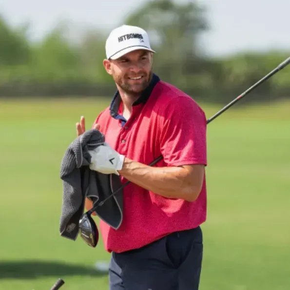 A man in a pink shirt is holding a golf club