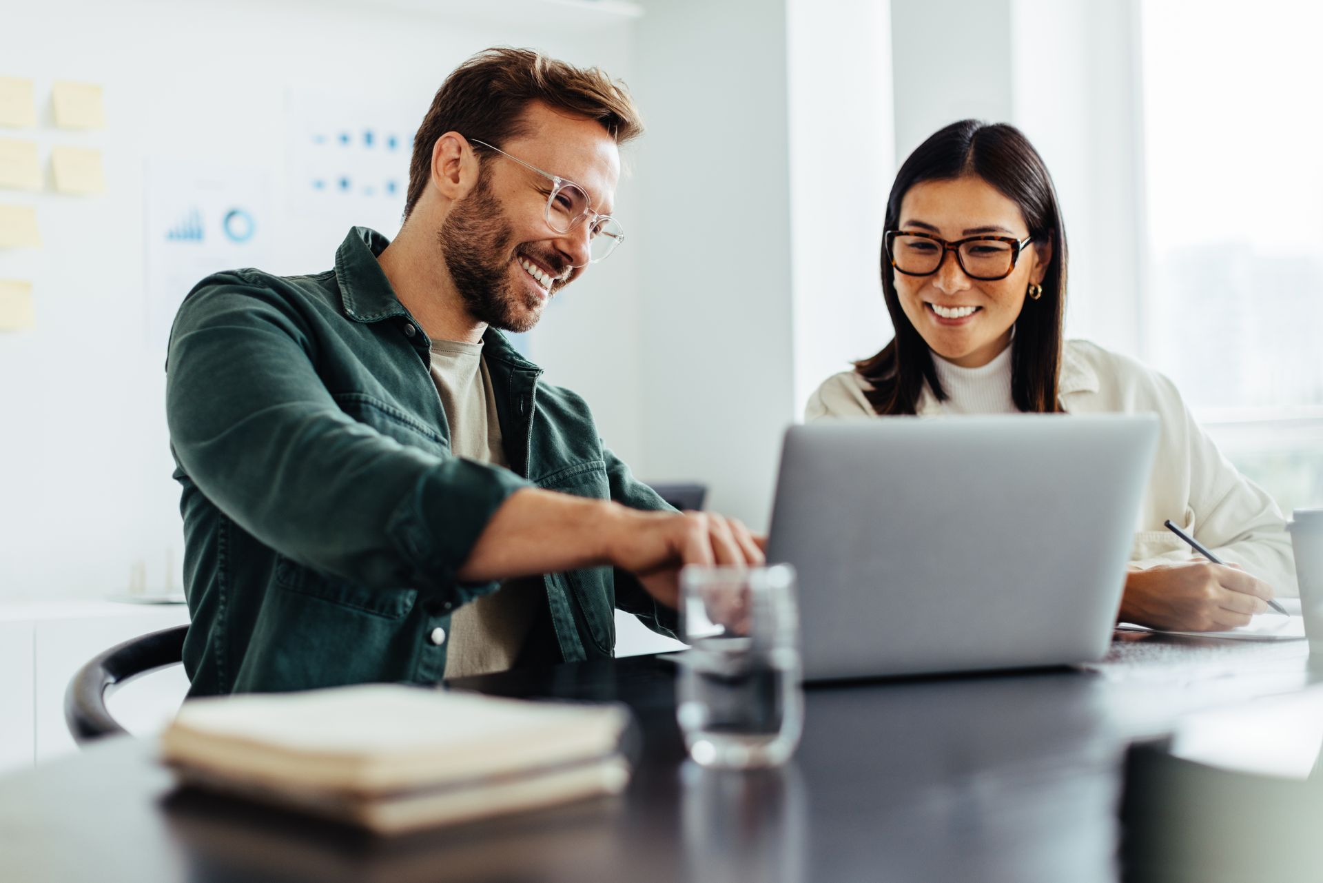 Man and woman smiling while working on a laptop in a modern office setting.