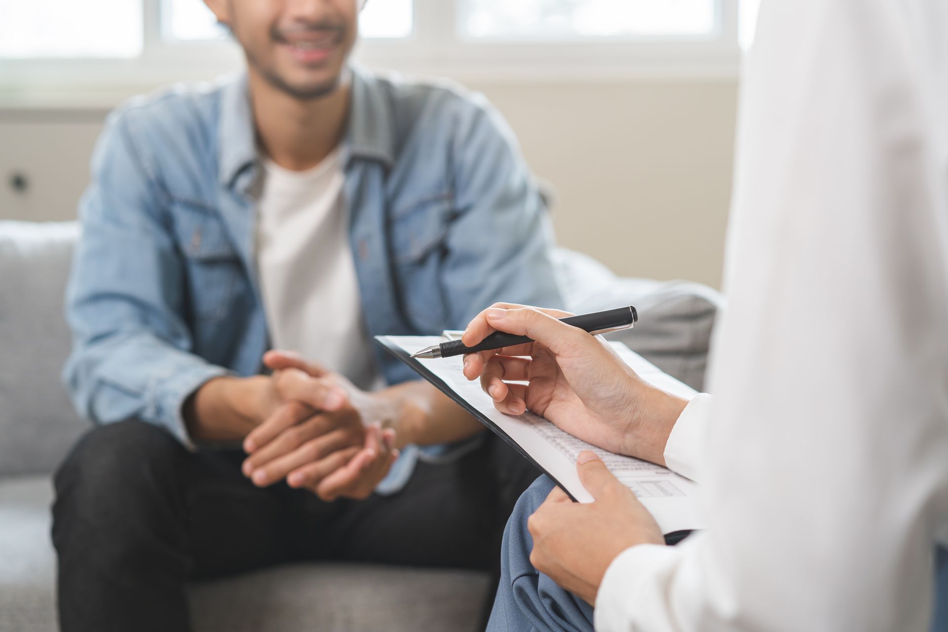 Man in therapy, smiling; therapist taking notes on clipboard.