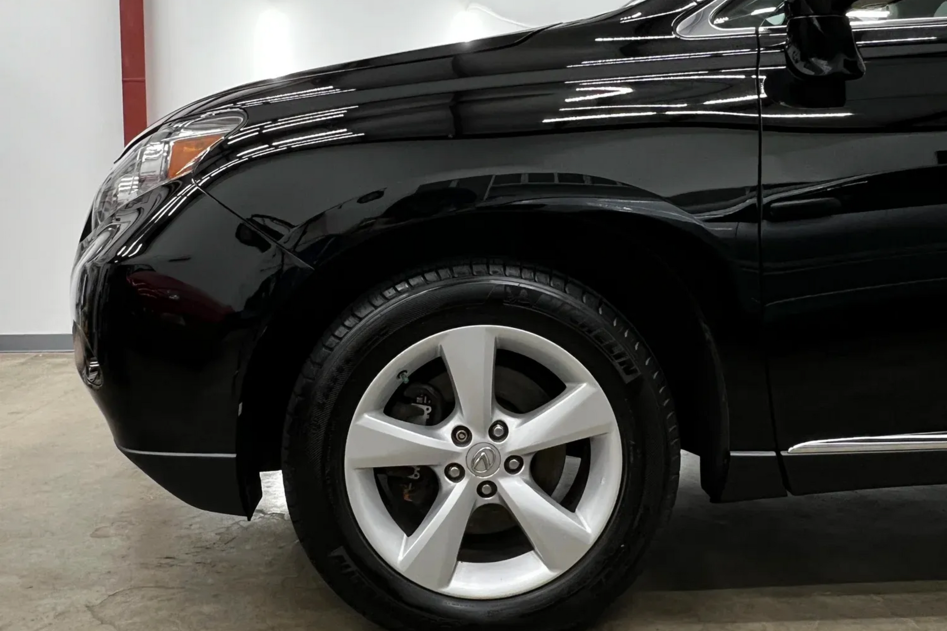 Black SUV front wheel and fender in a garage, with a silver alloy rim.
