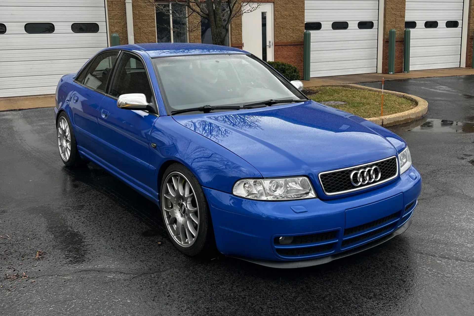 Blue Audi sedan parked on a wet driveway in front of a house and garage doors