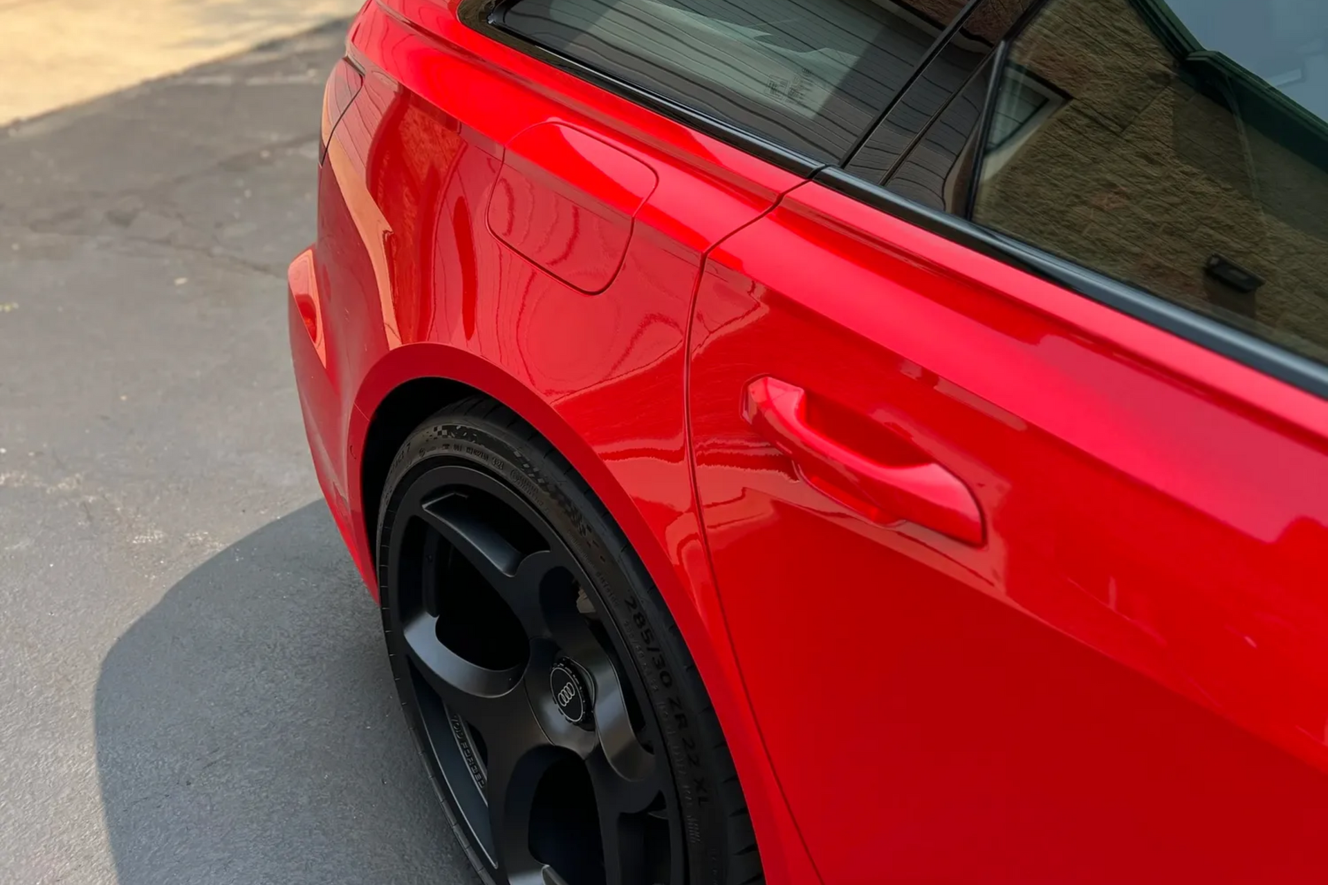 Close-up of a red sports car’s rear side with black wheel parked on pavement.