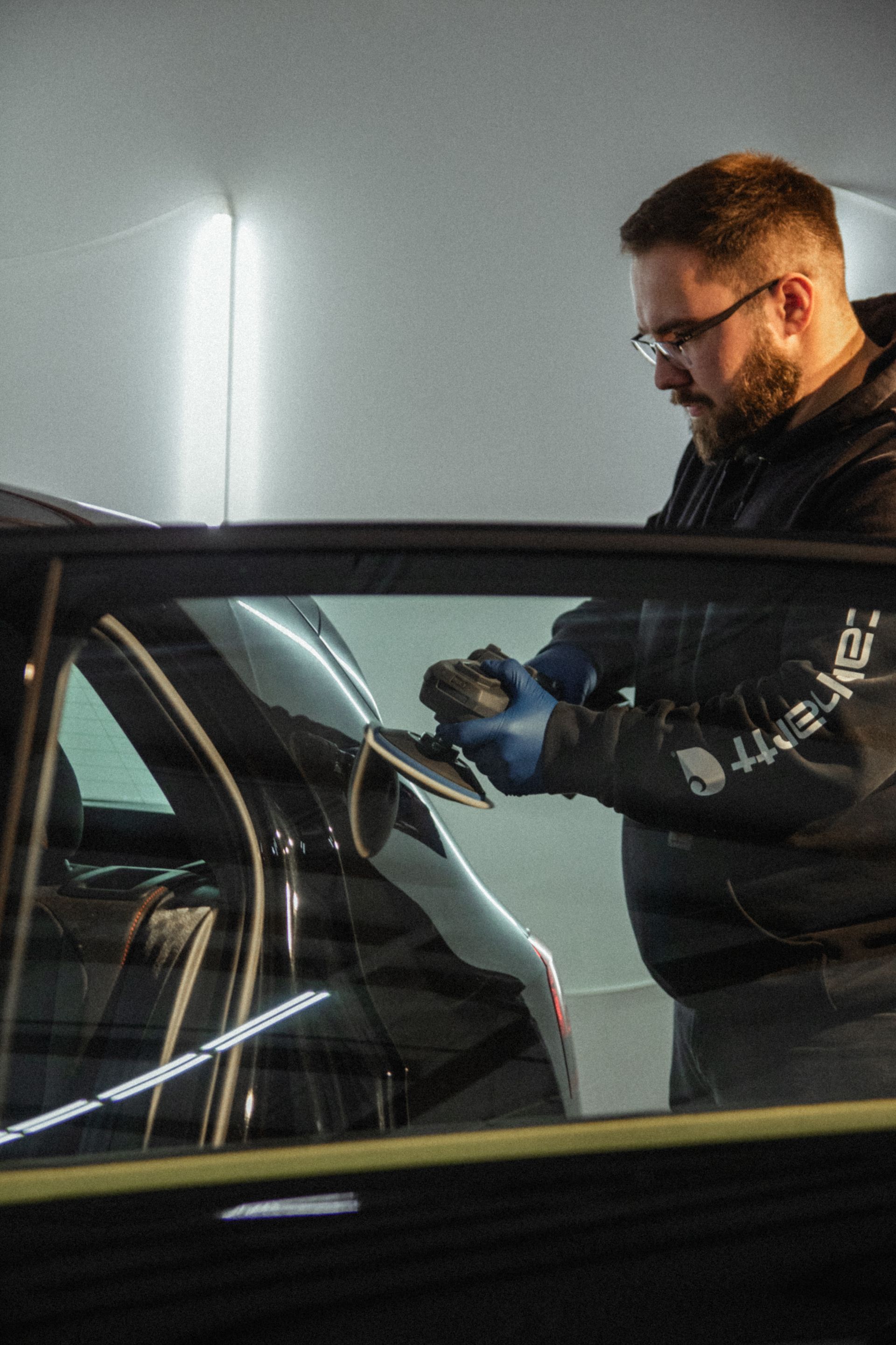 Man in blue gloves inspecting a car window indoors under bright lights