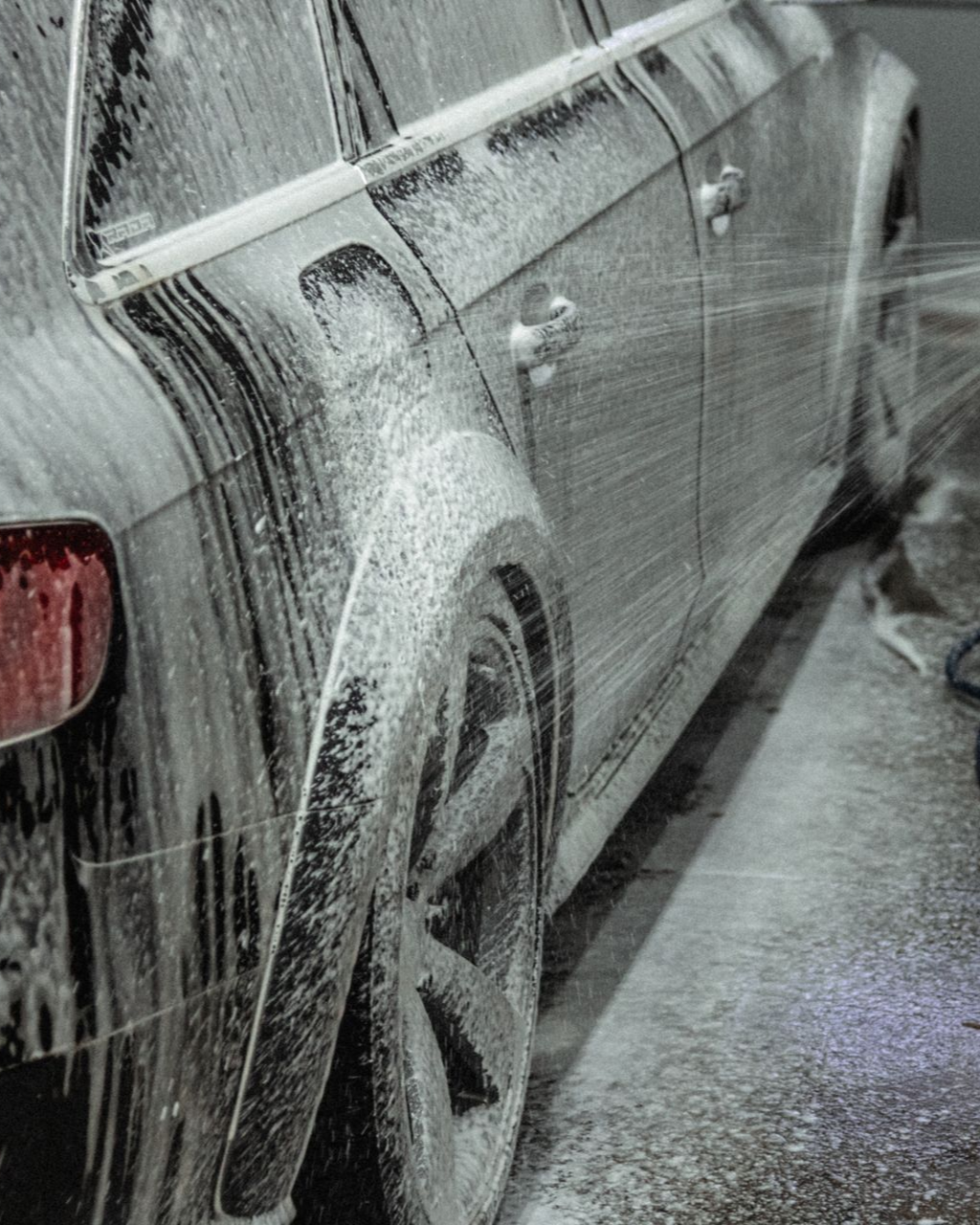 Car being washed with thick soap suds, close-up of the side and rear wheel.