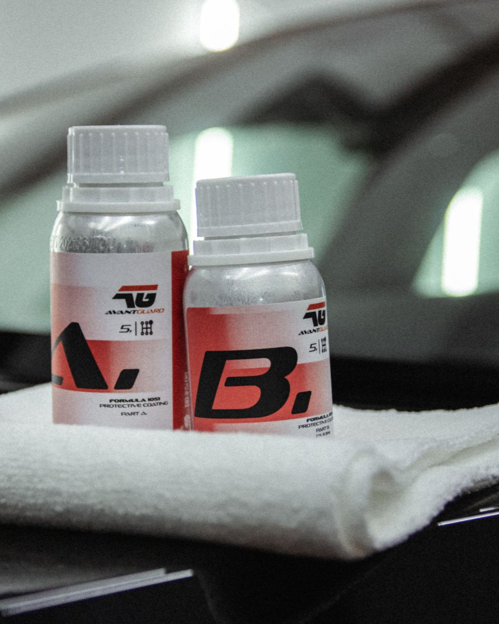 Two small white bottles with red labels on a white towel, in front of a blurred car interior.