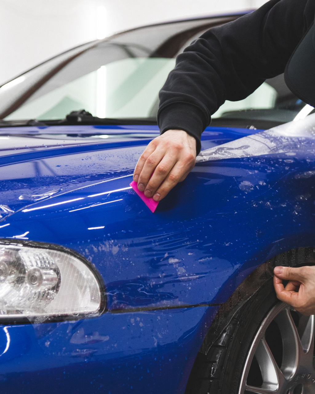 Person cleaning a blue car hood with a pink cloth, close-up view