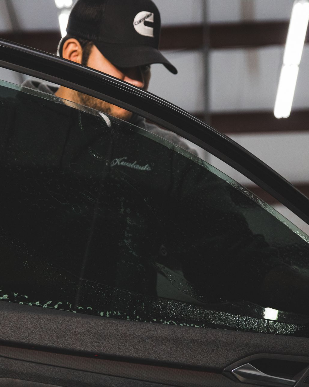 Man in a black cap working beside a car with the window half raised
