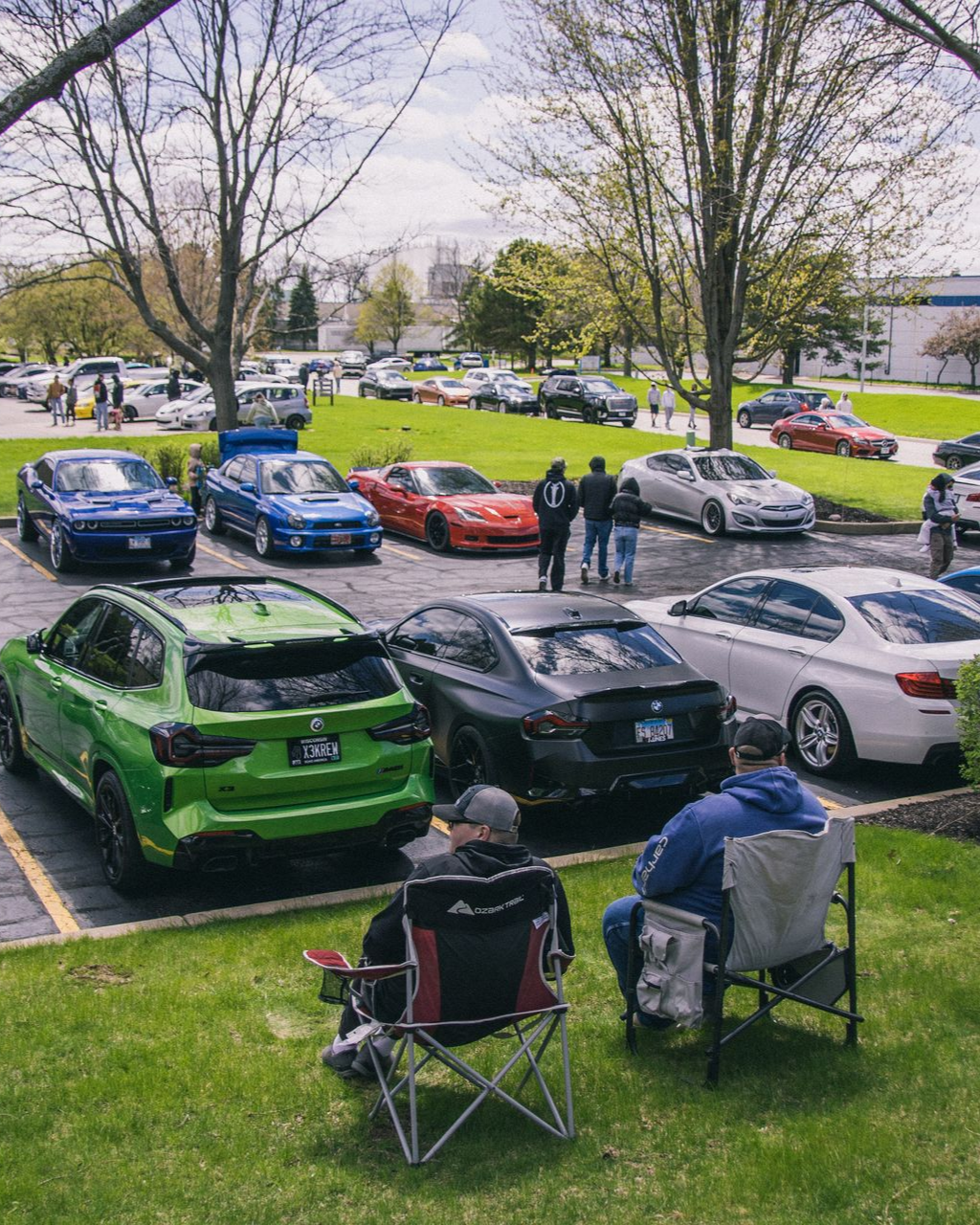 Row of colorful sports cars parked on grass with two people seated in folding chairs in the foreground.