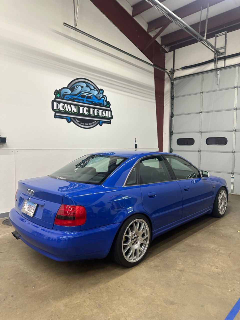 Blue sedan parked inside an auto shop with a wall logo and garage door in the background