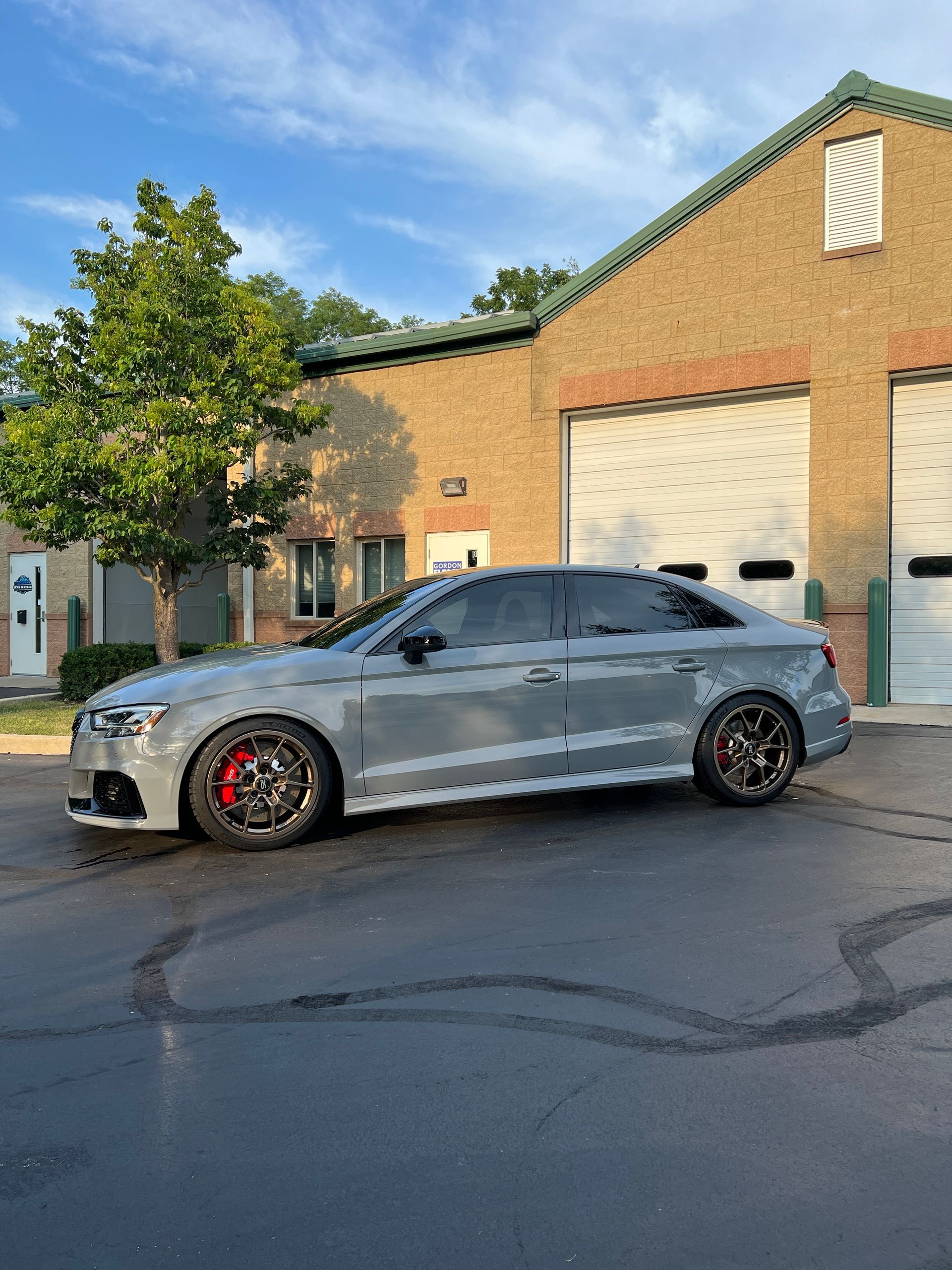 Gray sports sedan parked outside a brick industrial building at sunset.