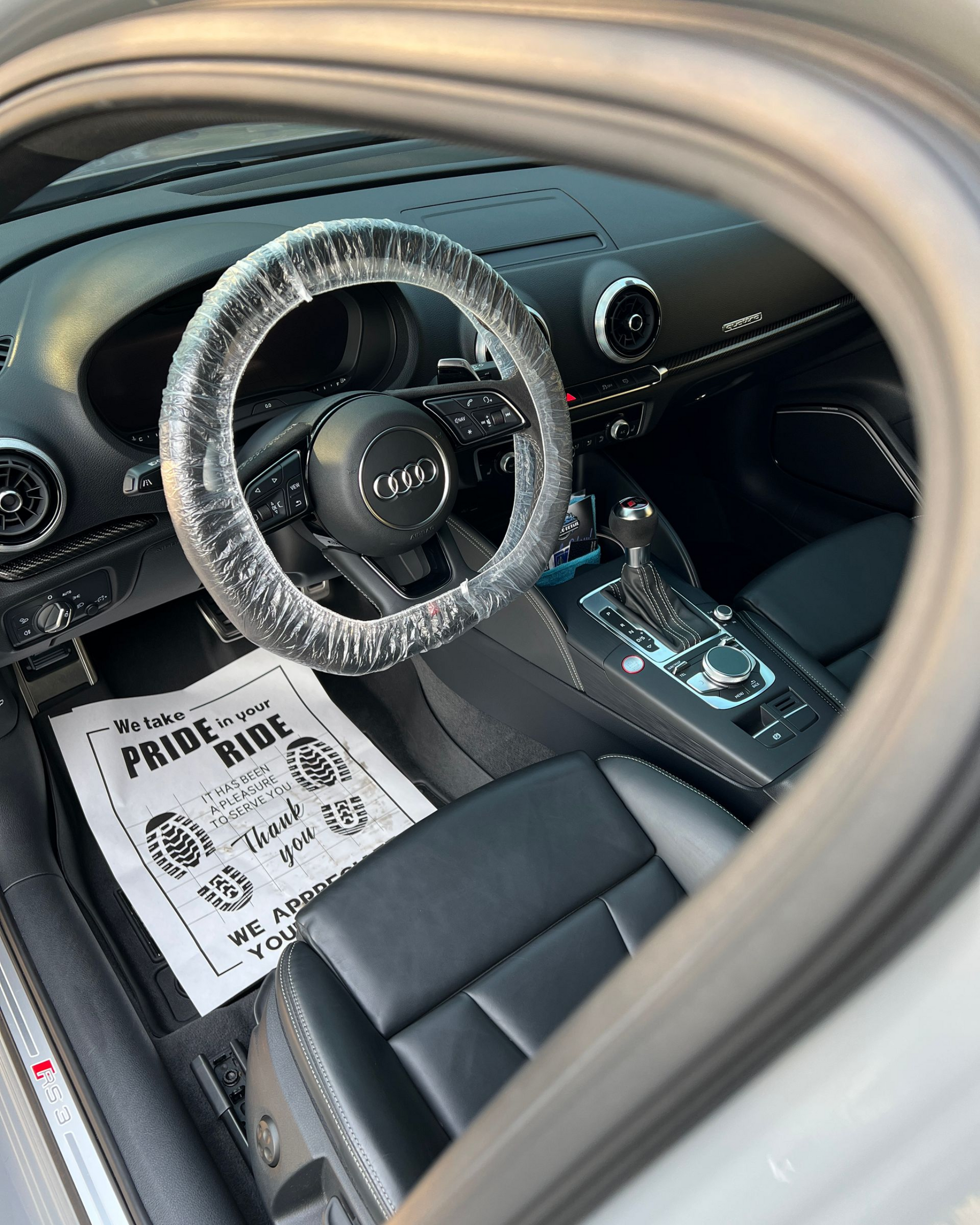 Car interior with black seats, steering wheel cover, and information sheet on the passenger seat.