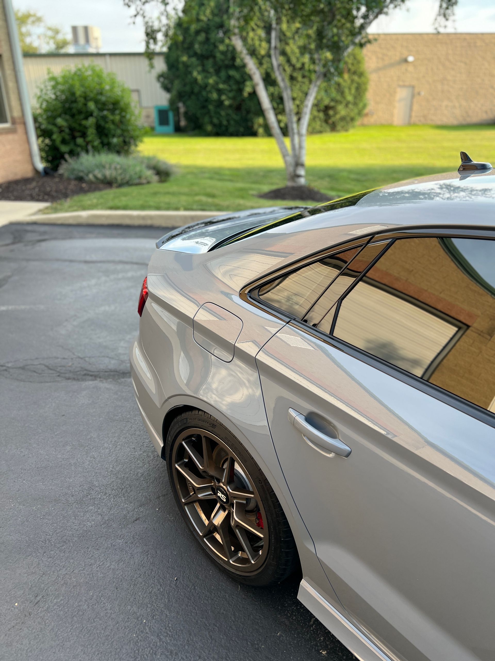 Silver sports car parked on a suburban street, rear side view, with dark alloy wheels.