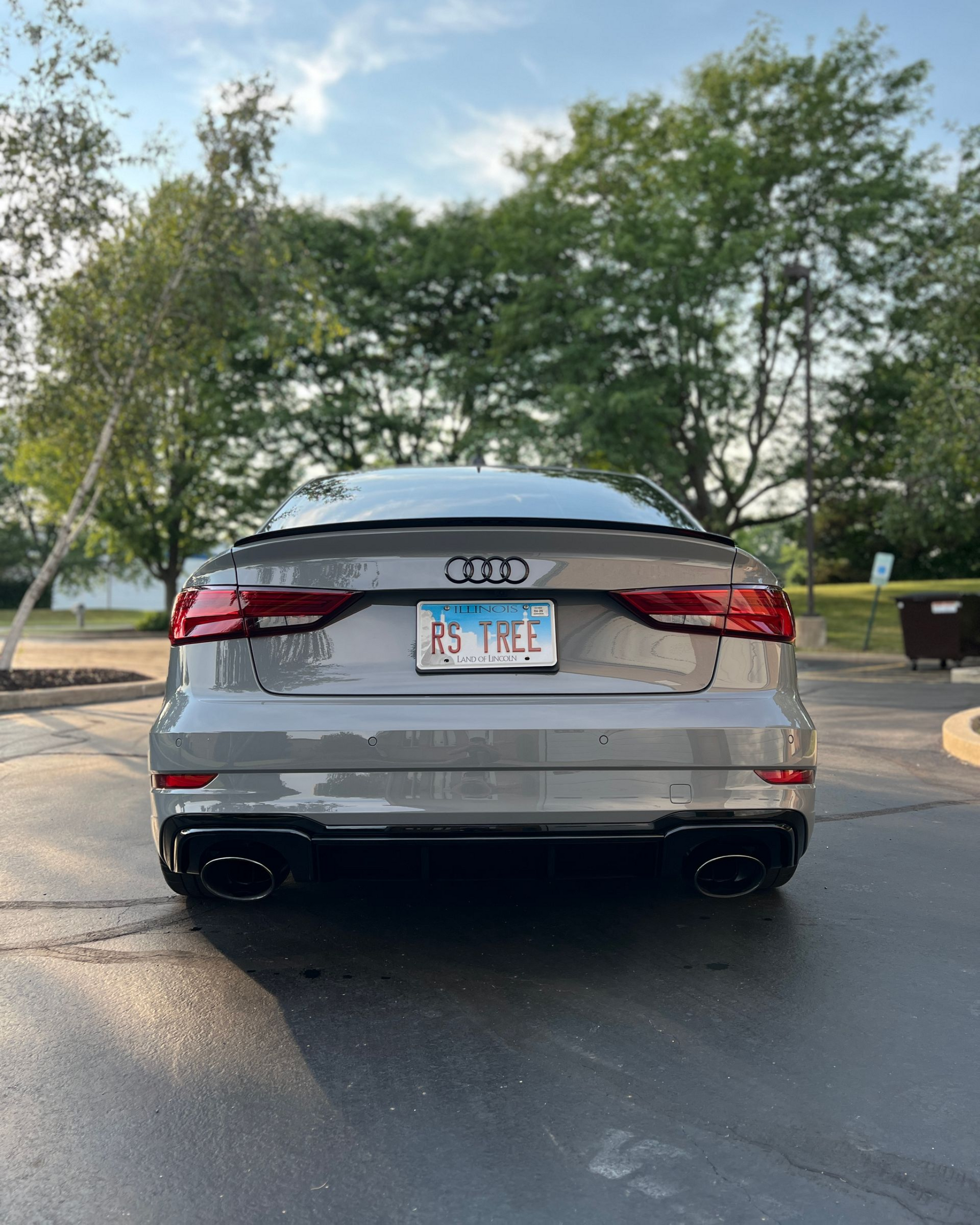Silver Audi SUV viewed from the rear on a road, with trees and a partly cloudy sky in the background