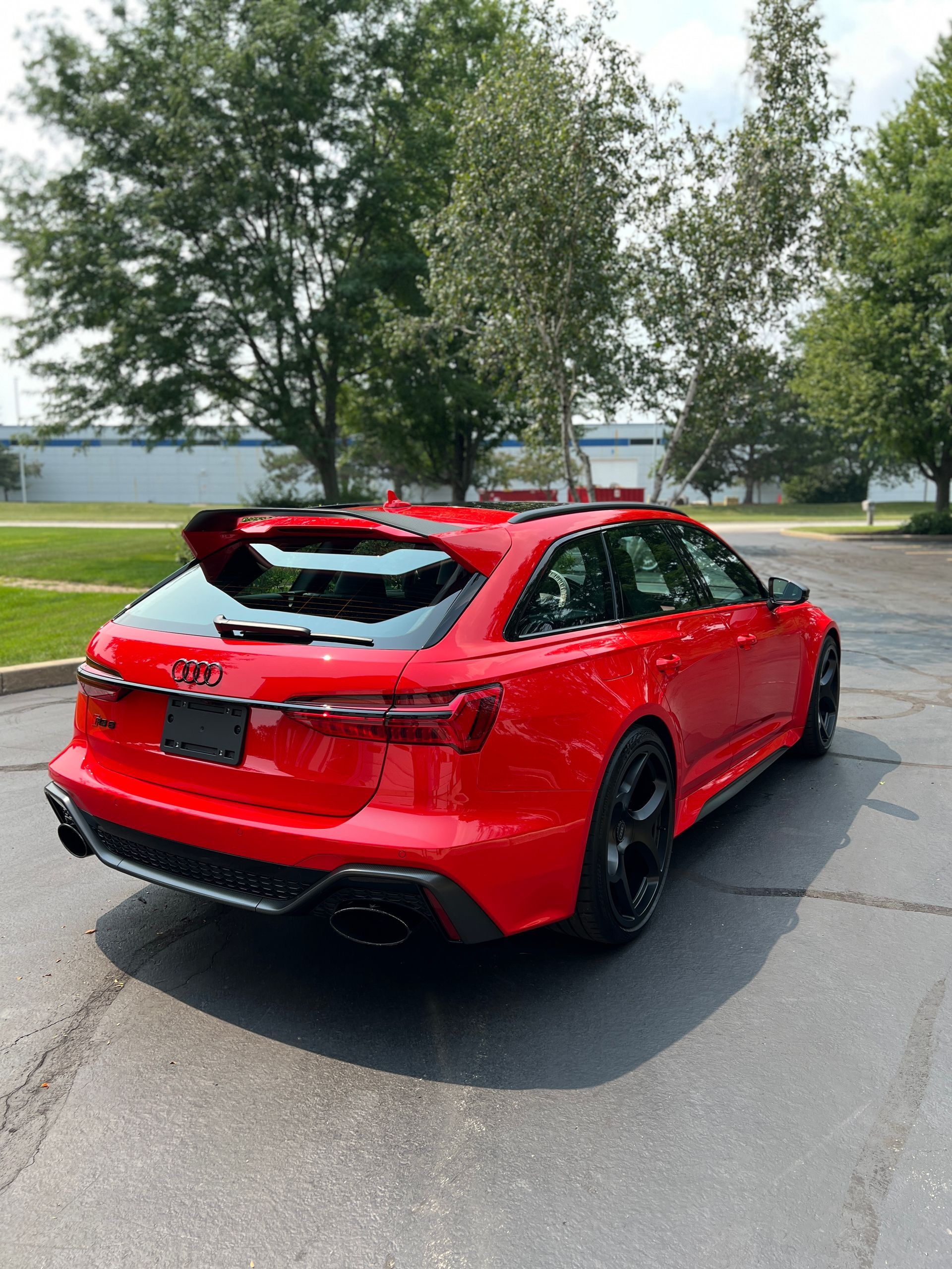 Red Audi sedan parked on a street beside trees and a waterfront on a sunny day