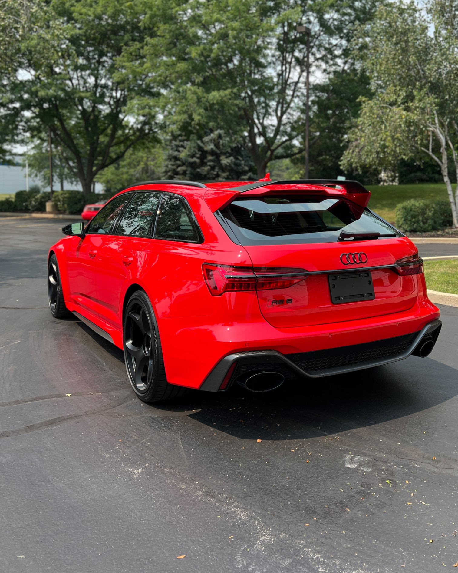Red sports hatchback parked on wet pavement with trees in the background.