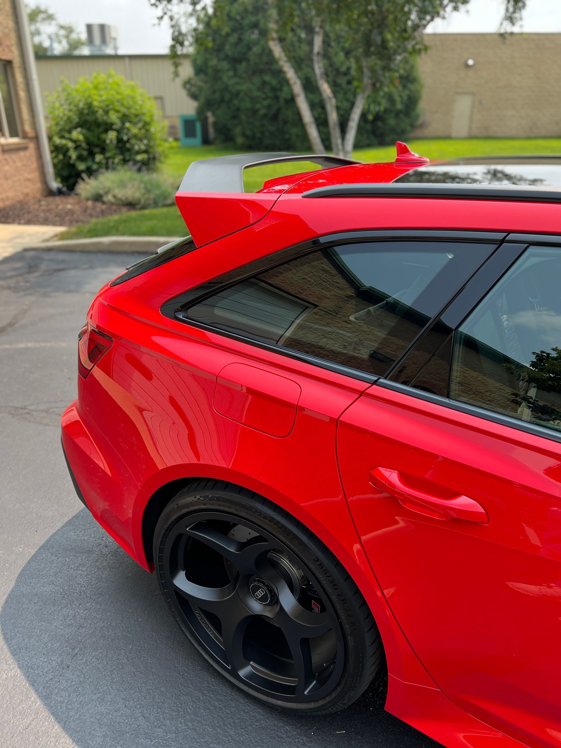 Red sports coupe parked on a suburban street, rear side view, with black wheels and a rear spoiler.