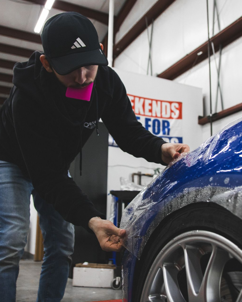 Person applying blue film to a car fender in a workshop