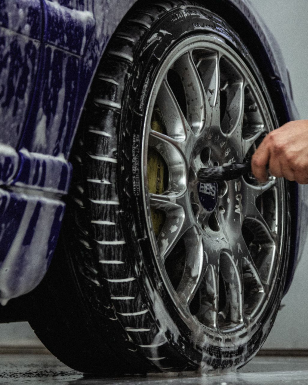 Hand washing a purple car wheel with soap and a brush