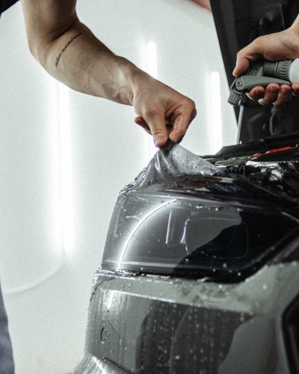 Hands apply protective film to a car headlight in a workshop