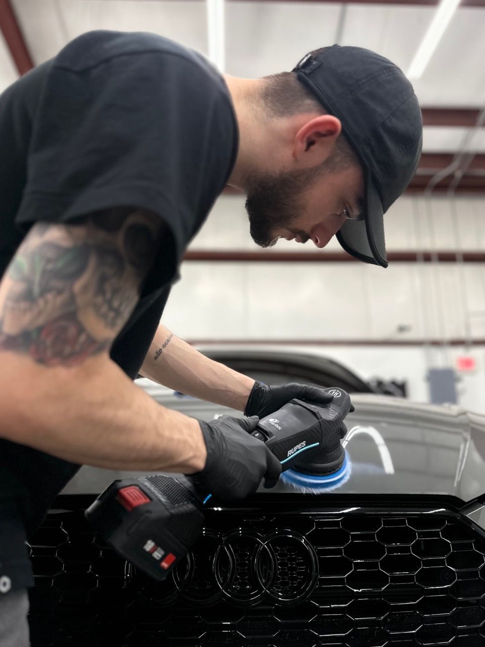 Mechanic polishing a black car grille with a buffer in an auto shop