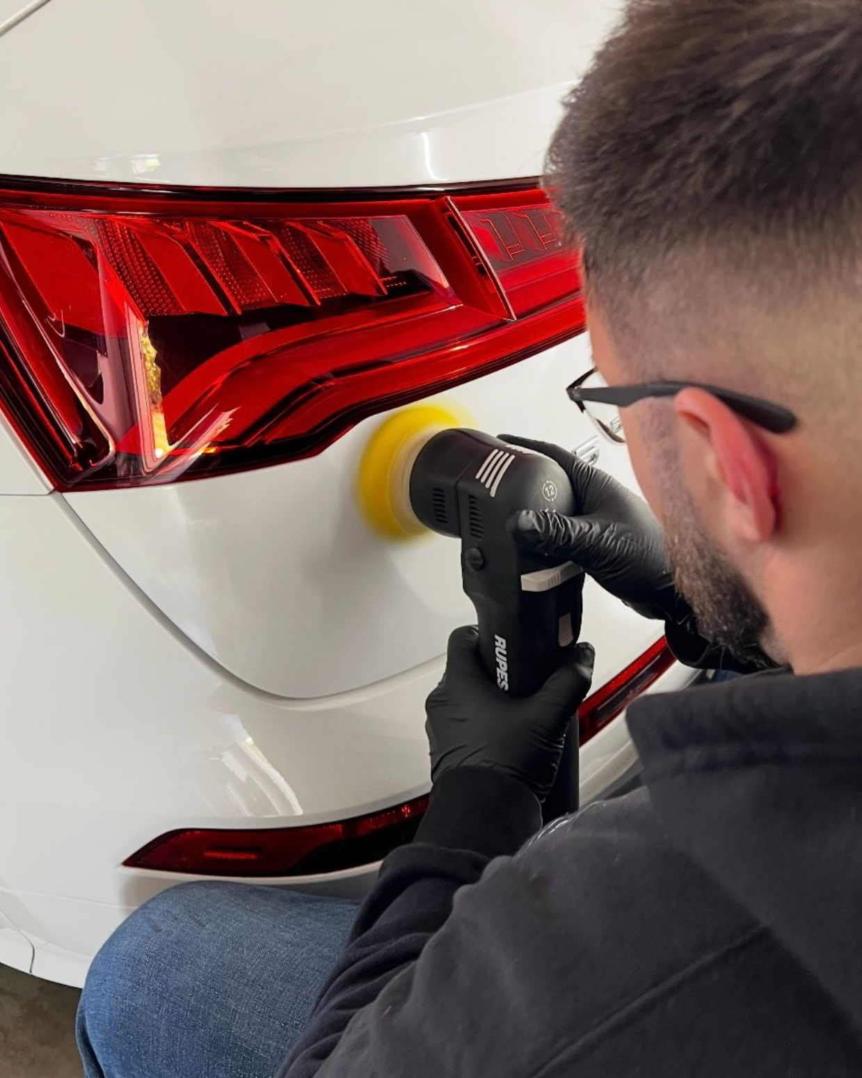 Mechanic polishing a white car’s red taillight with a power buffer