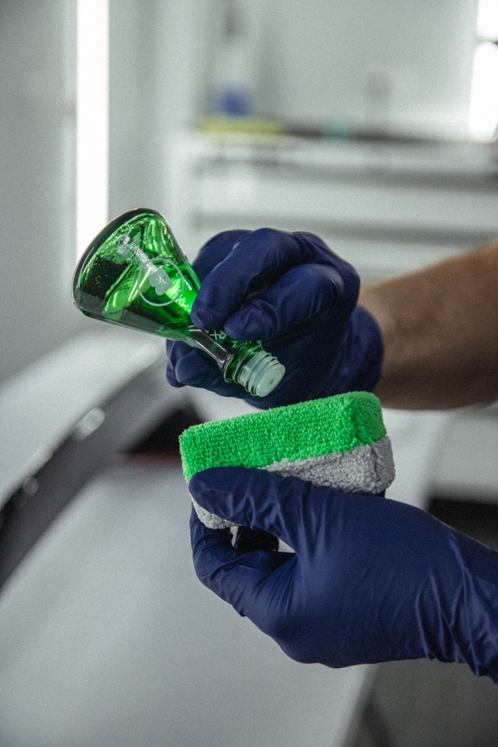 Gloved hands hold a green toothbrush and scrub a white-and-green sponge in a sink area.