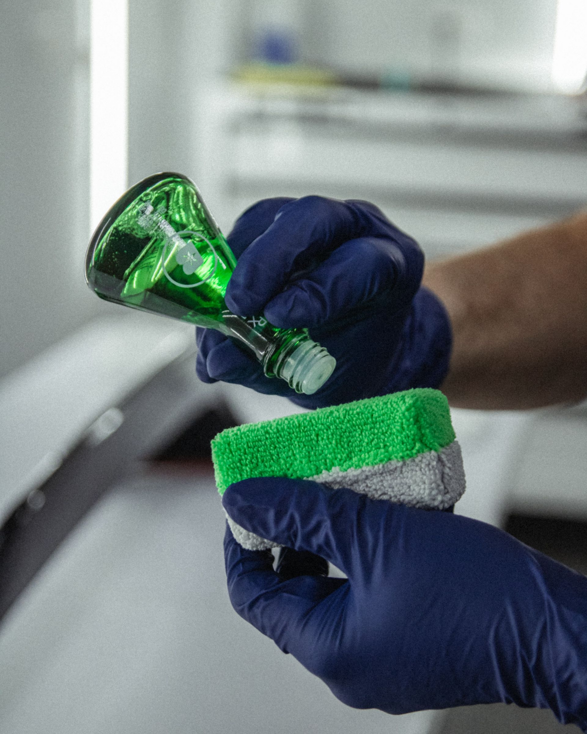 Gloved hands apply green cleaner to a scrub sponge in a kitchen-like setting