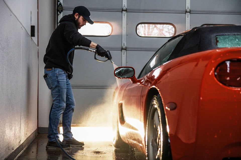 Person washing a red car with a hose in a garage
