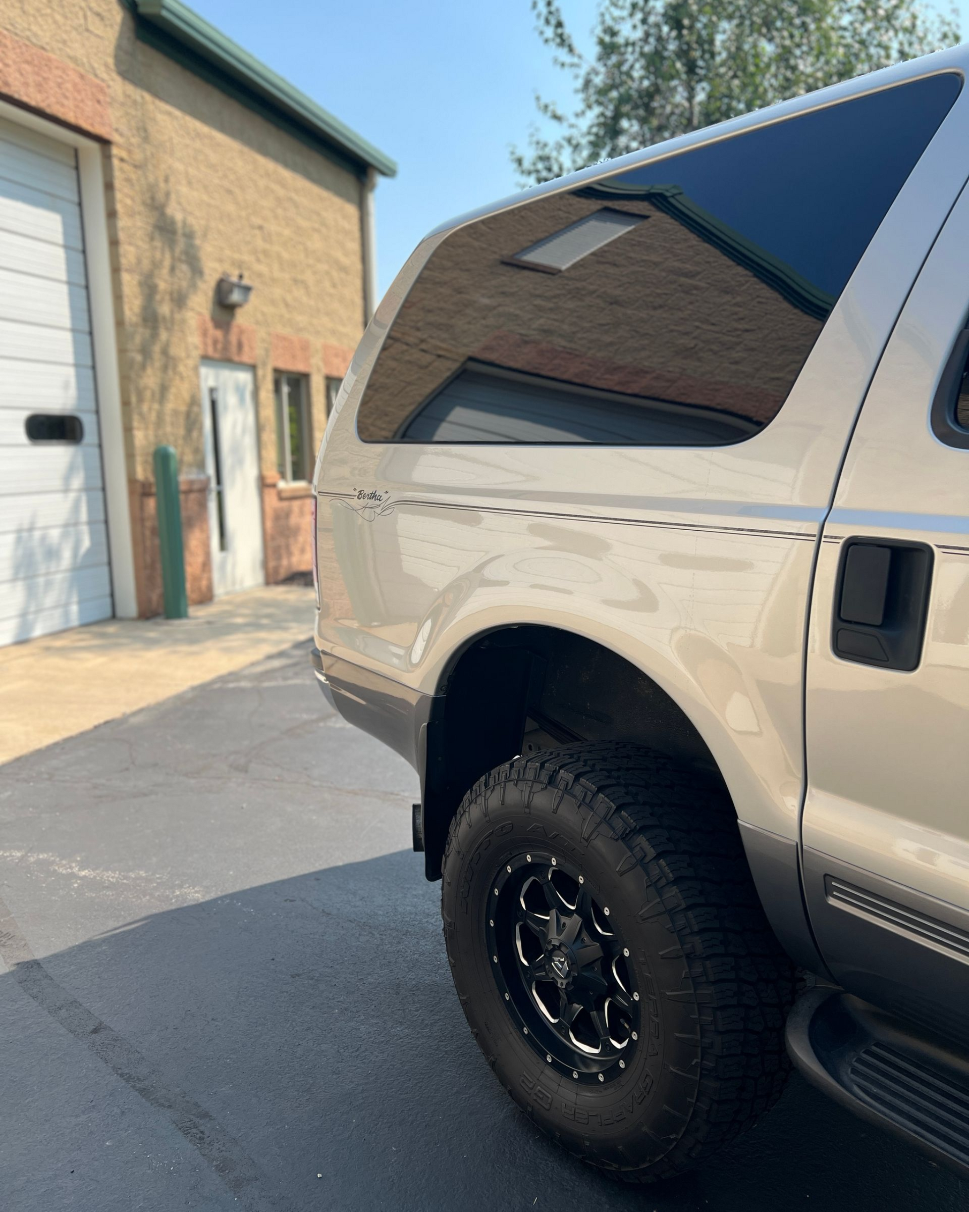 White pickup truck parked beside a brick building in a driveway, rear side view