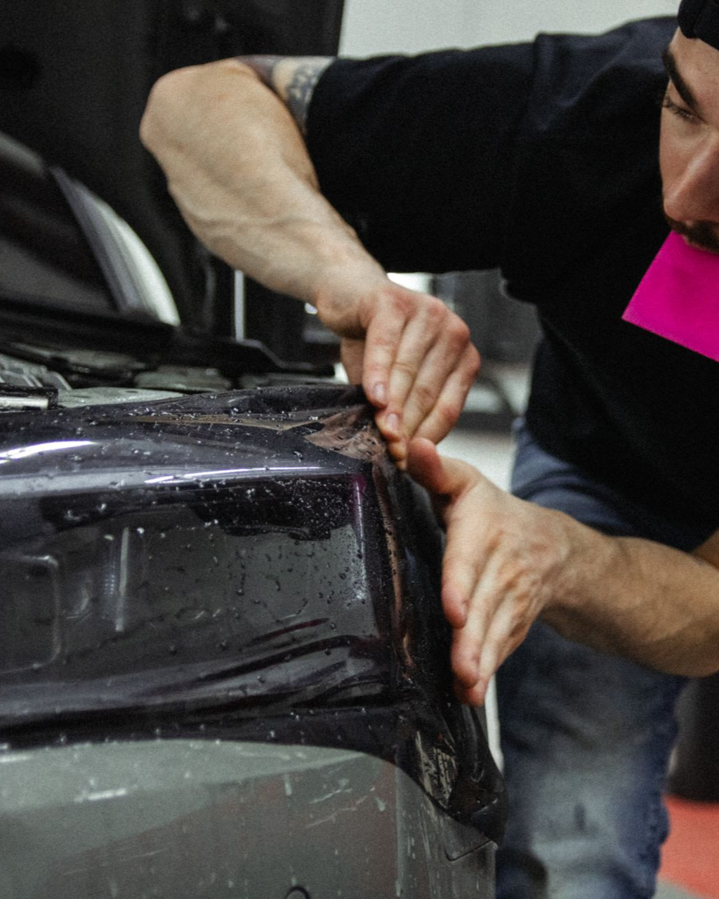 Person applying film to the corner of a black car window with a tool