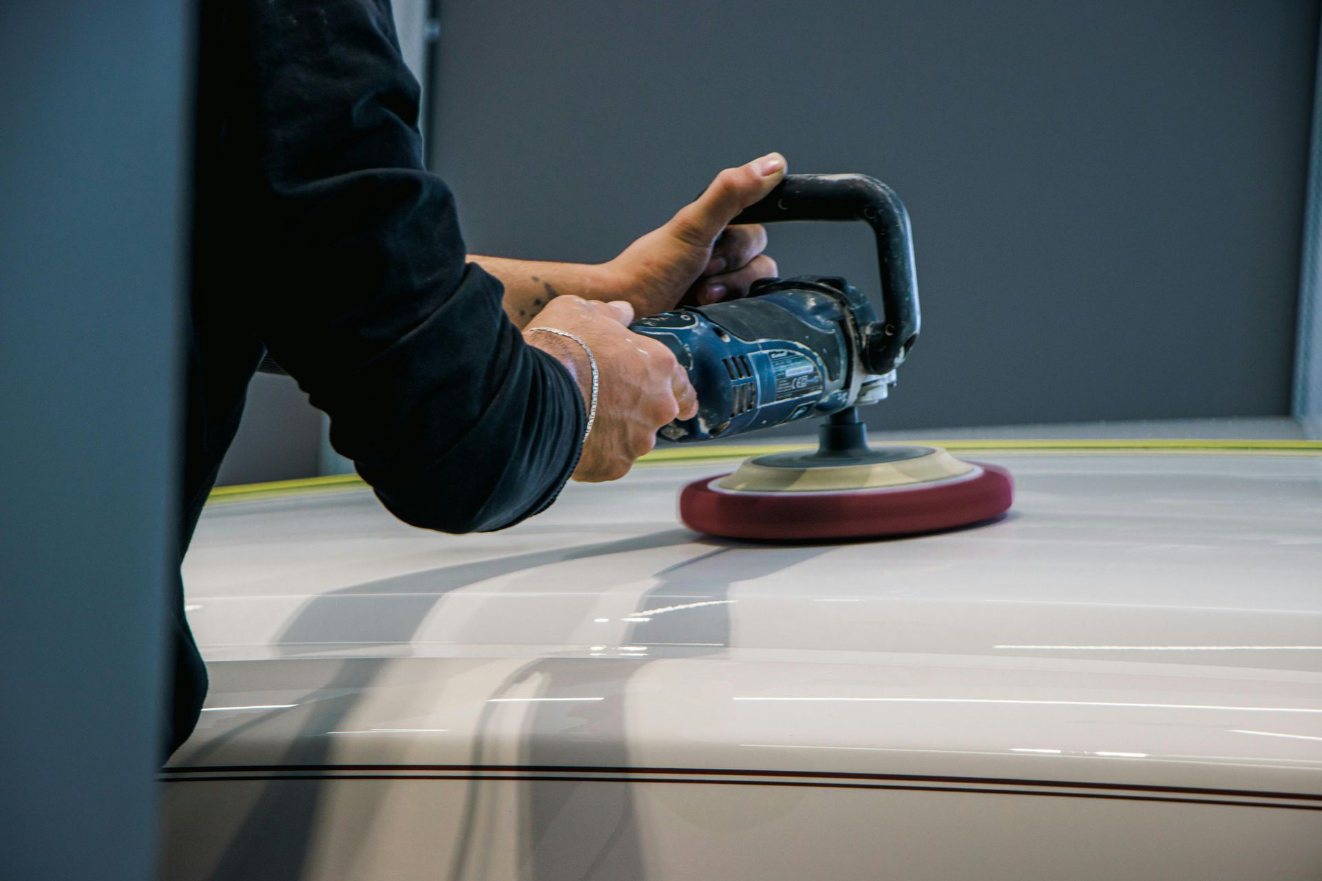 Person polishing a white car hood with a handheld buffer