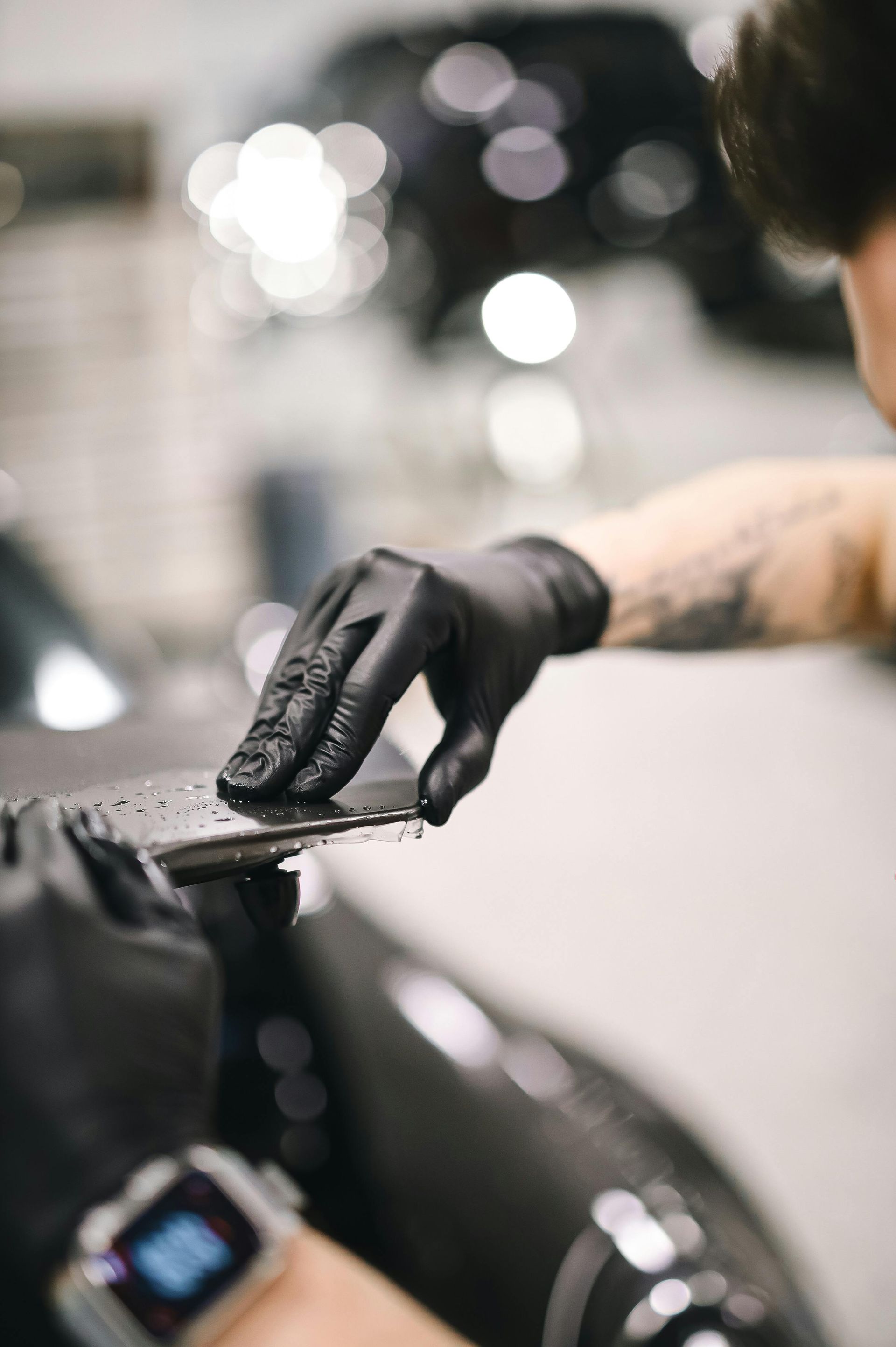 Gloved hand applying wax to a black car hood in a workshop