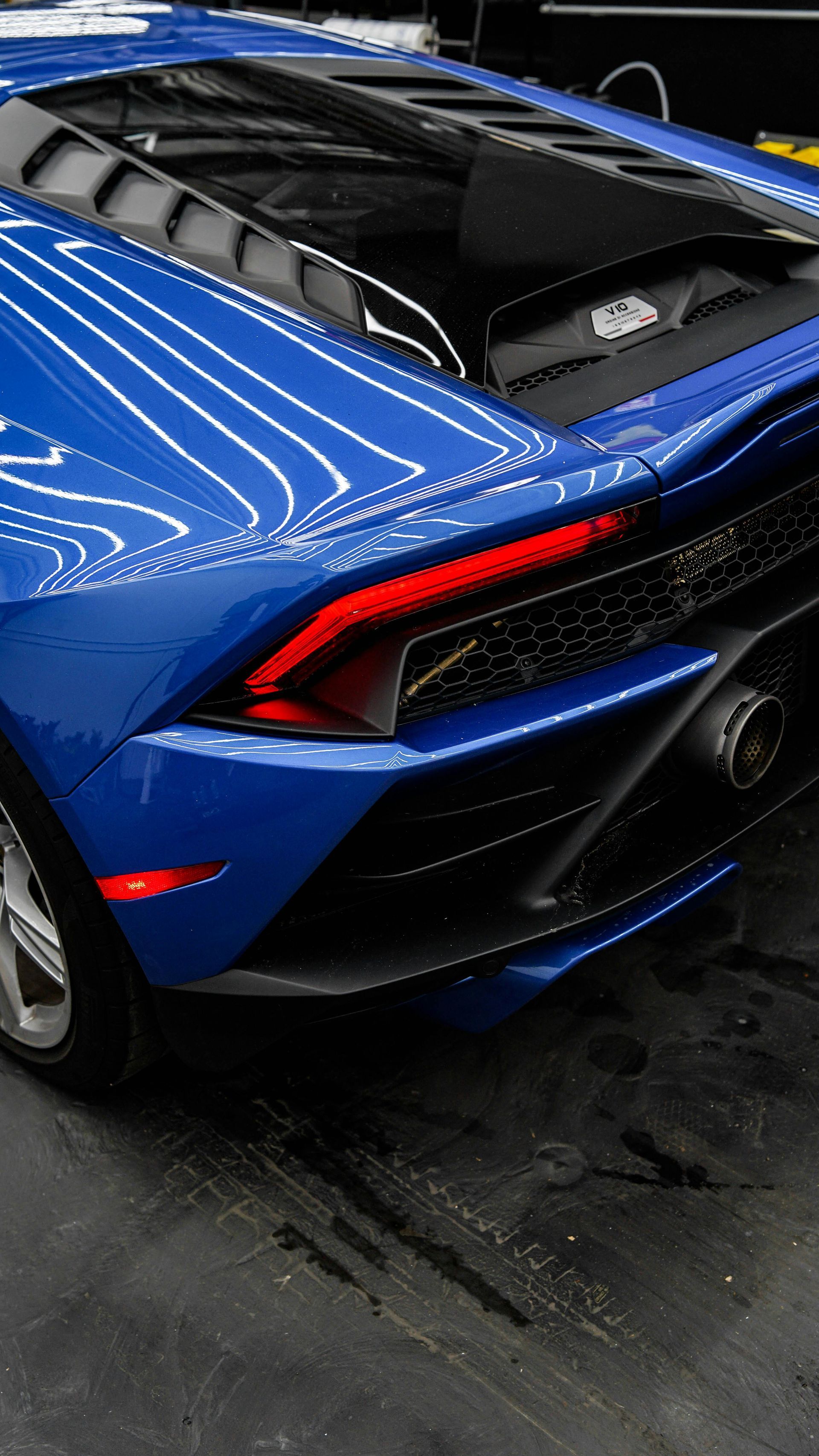 Blue sports car with black roof and red taillight, viewed from the rear in a garage.