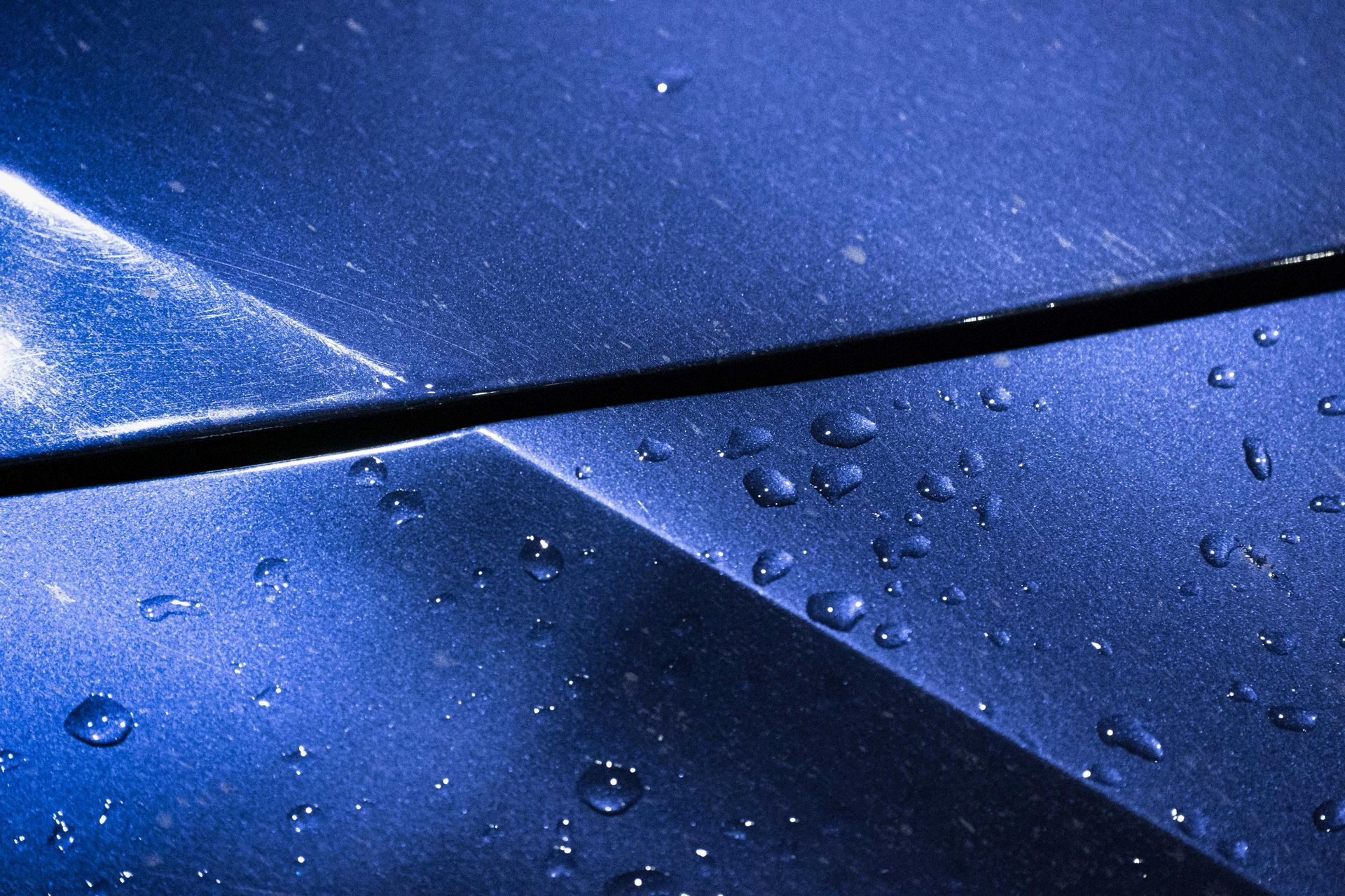 Blue car hood with raindrops and reflections