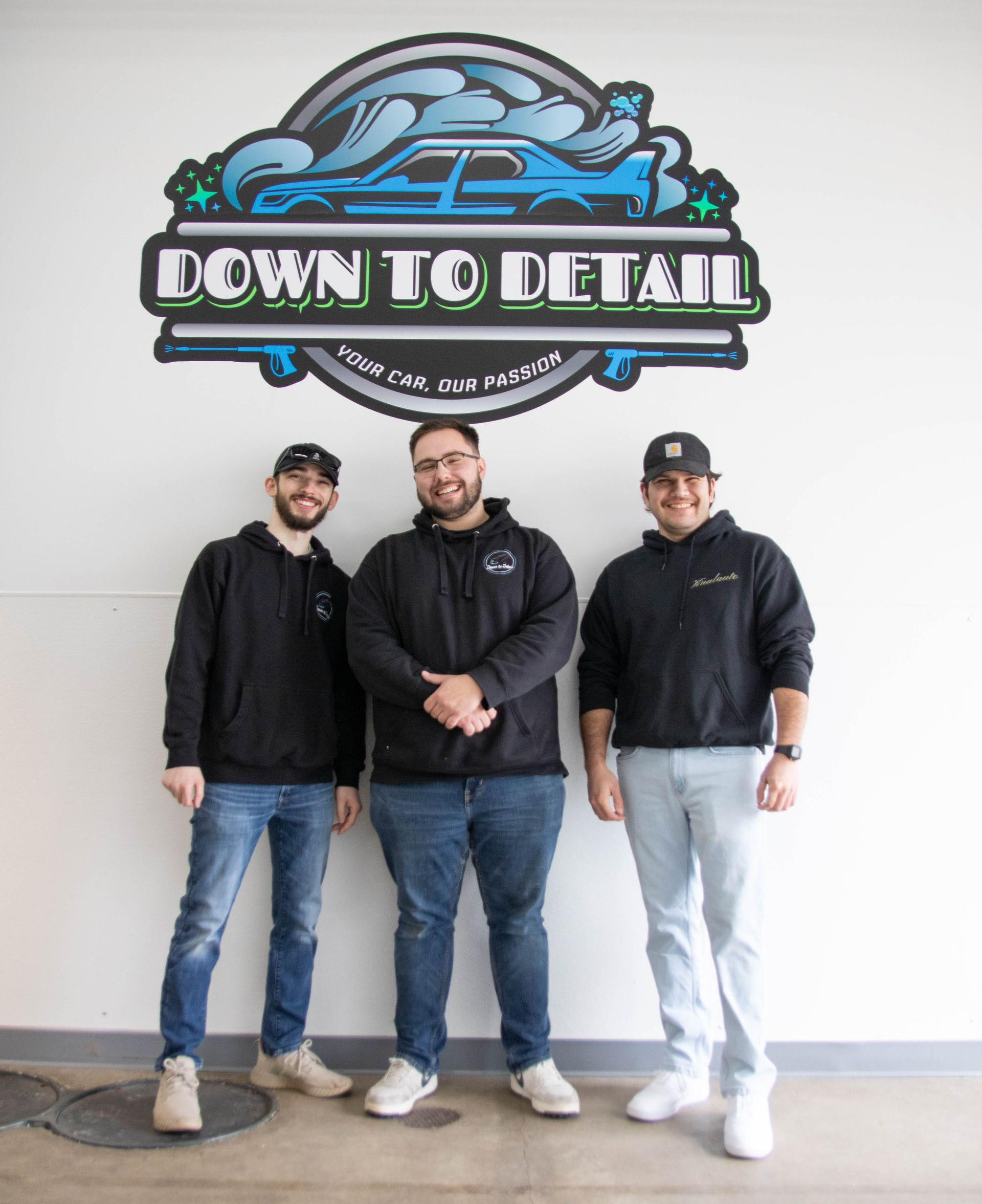 Three people in black hoodies standing under a “Down to Detail” wall sign