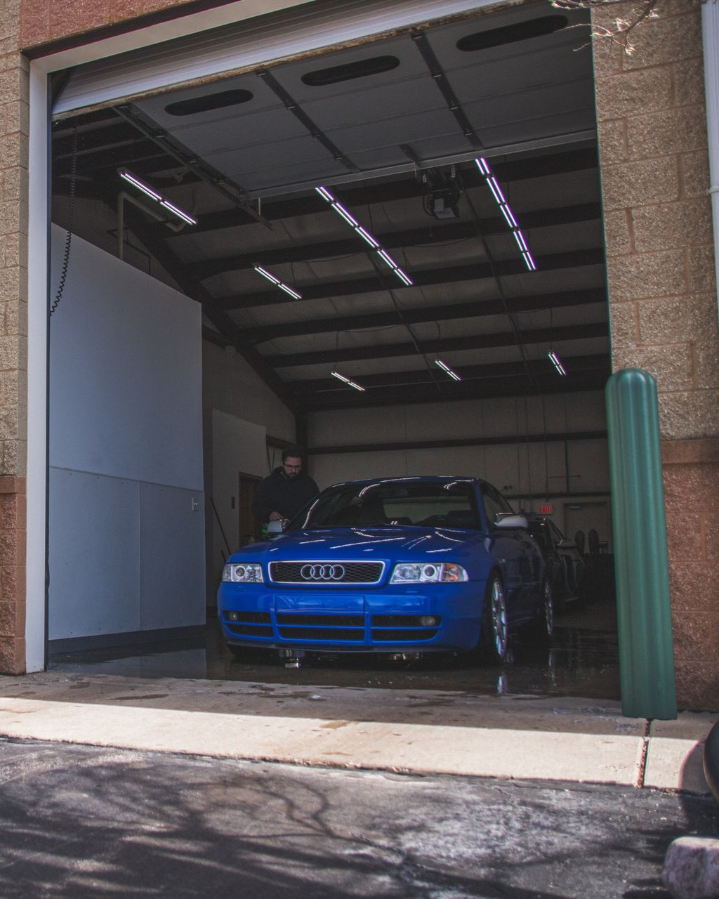 Blue Audi sports car parked in a garage doorway, with a person standing beside it.