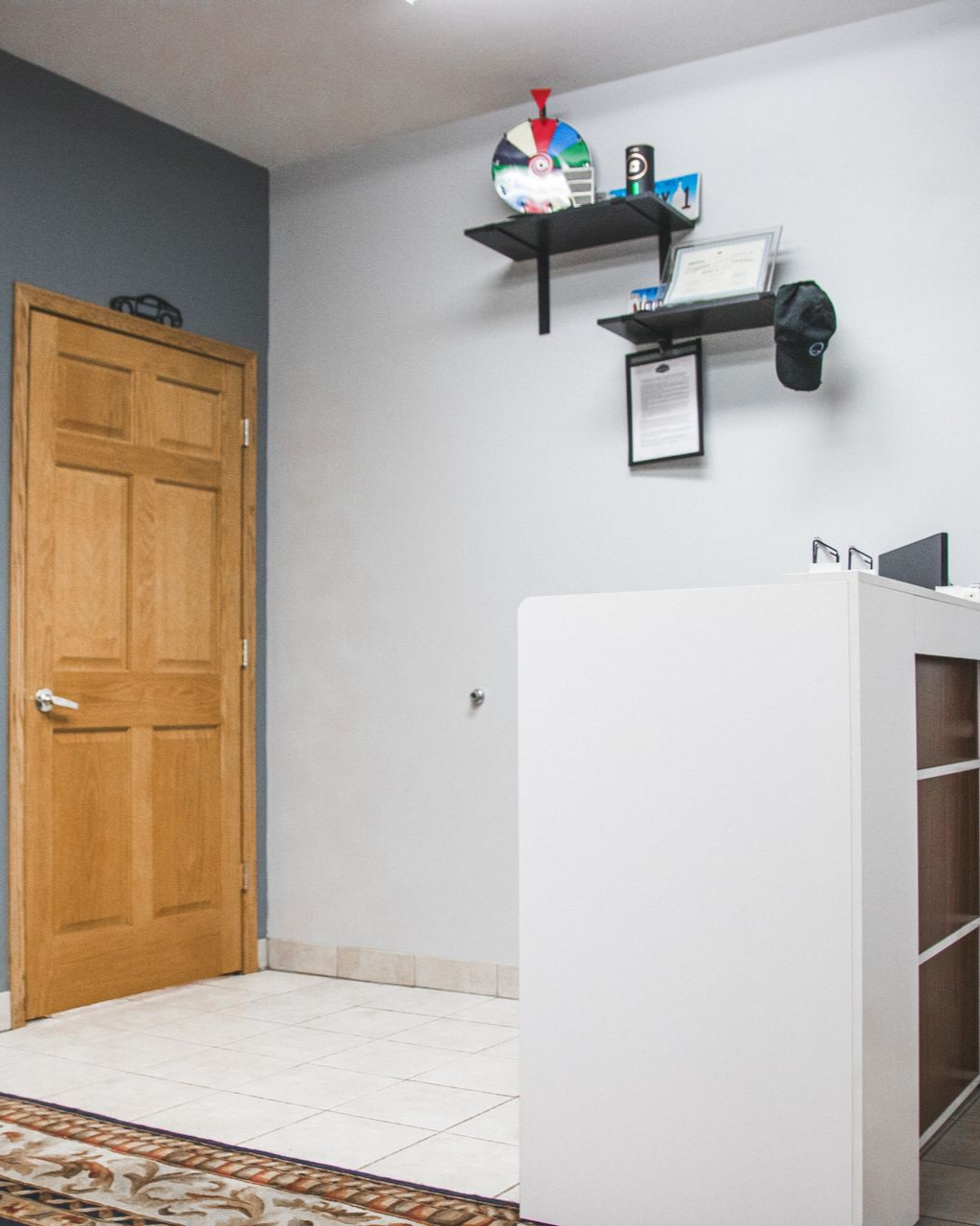 Small room interior with a wooden door, wall shelf, desk, and white cabinet.