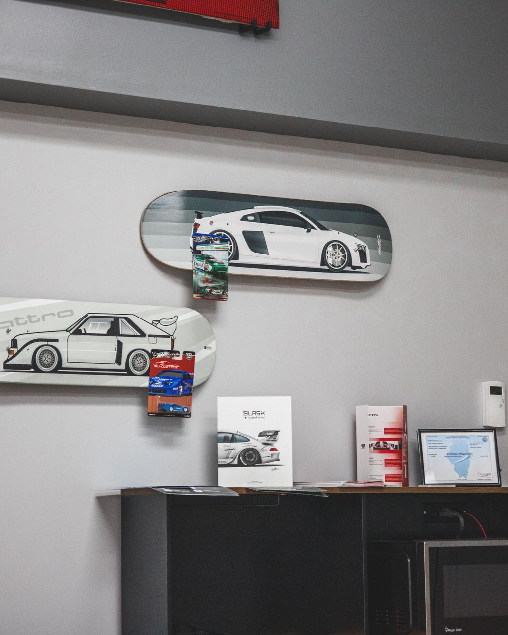 Wall with framed car artwork above a black cabinet in an office-like room