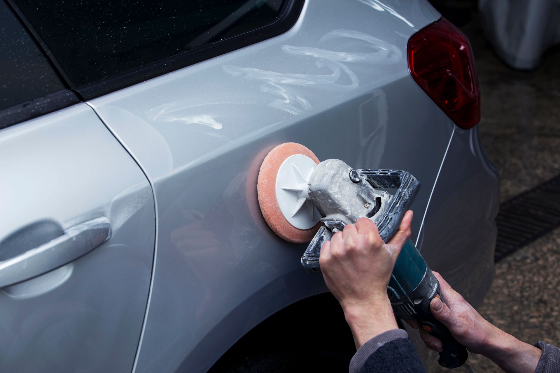 Hand using a power buffer to polish the gray side of a car