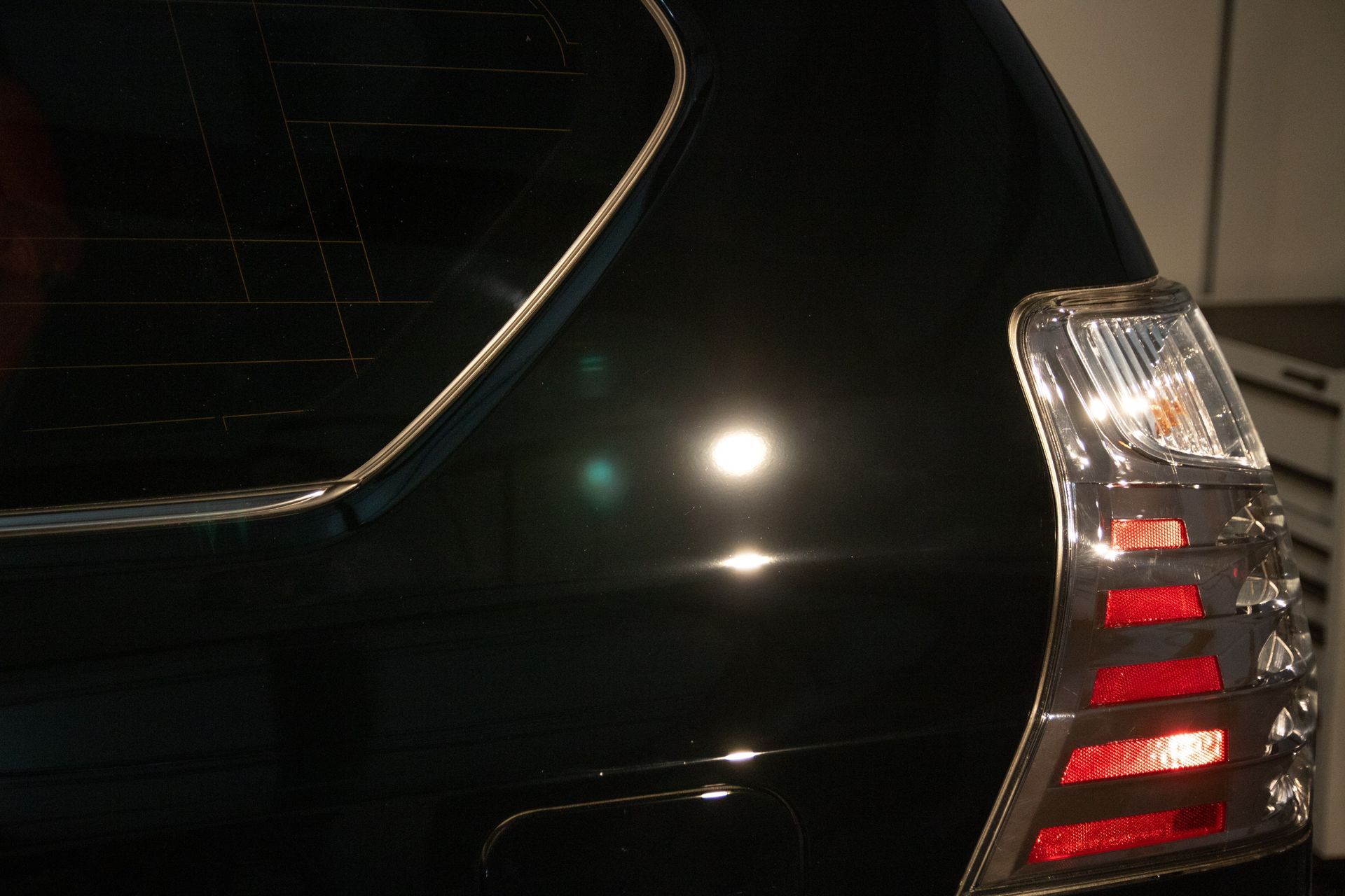 Close-up of a black car’s rear corner with red taillight illuminated