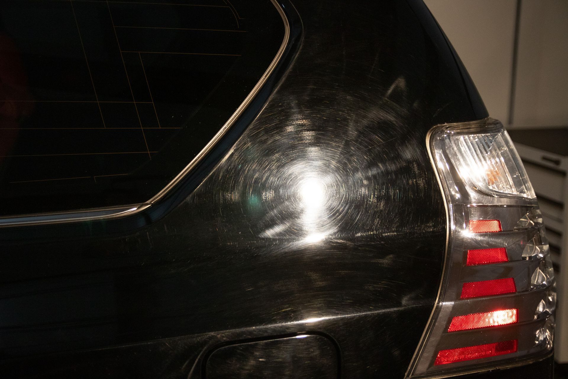 Rear corner of a black car with a taillight visible at night