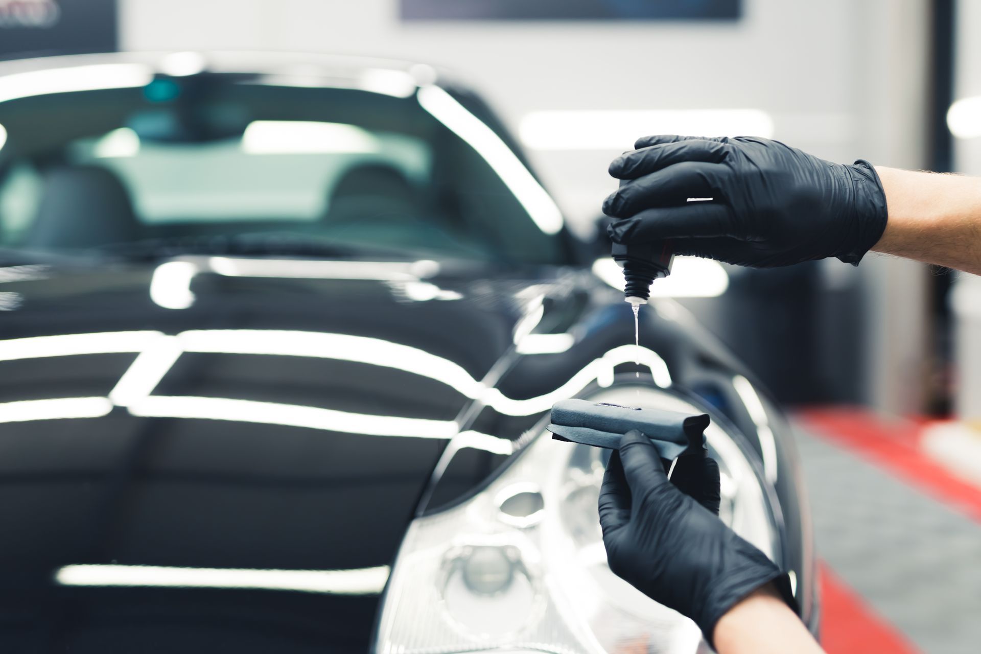 Gloved hands polishing a black car with a detailing cloth in a garage