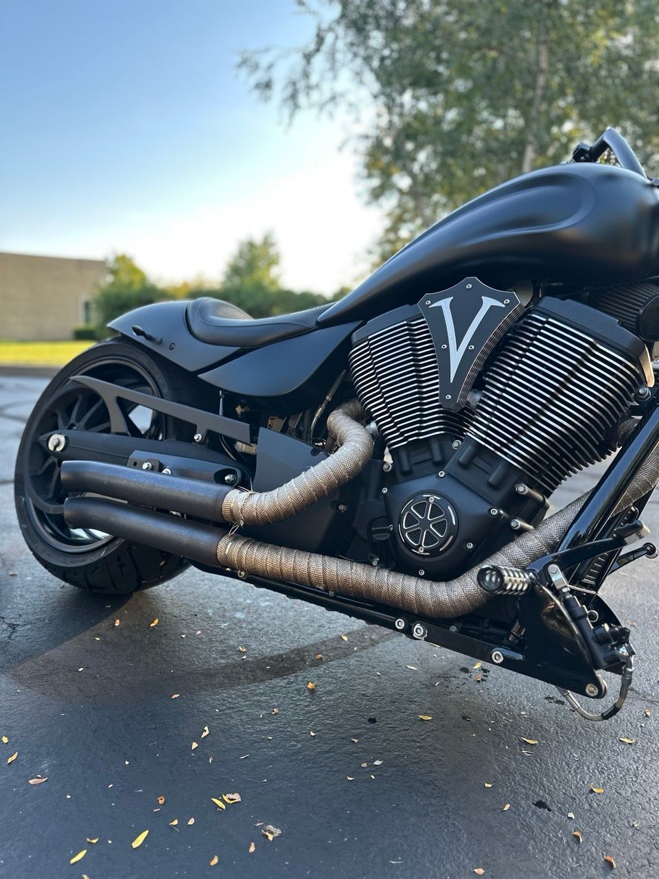 Black custom V-twin motorcycle with rusty exhaust parked on pavement outdoors