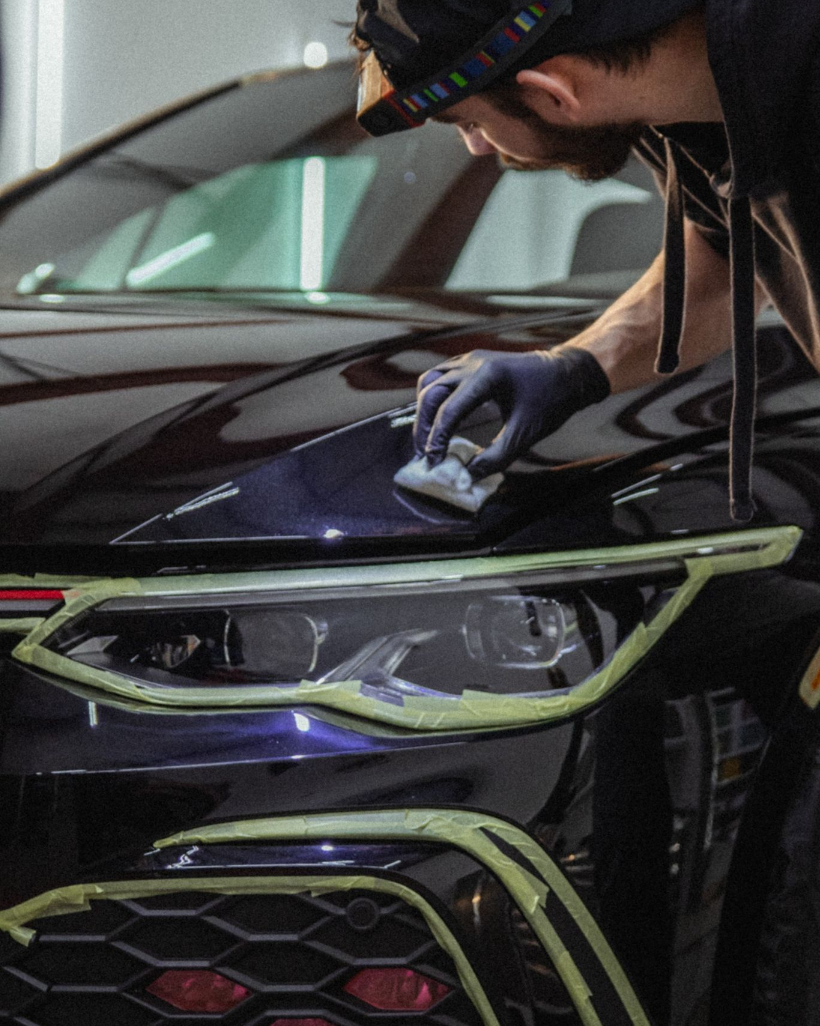 Person polishing the hood of a black car with neon green trim in a garage
