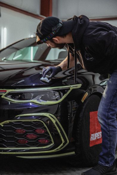 Person polishing the front of a black car in a garage with neon green trim