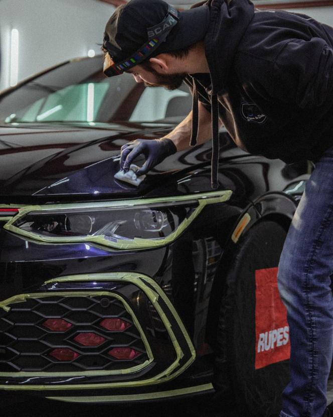 Person wipes the hood of a black car with a cloth in a garage.