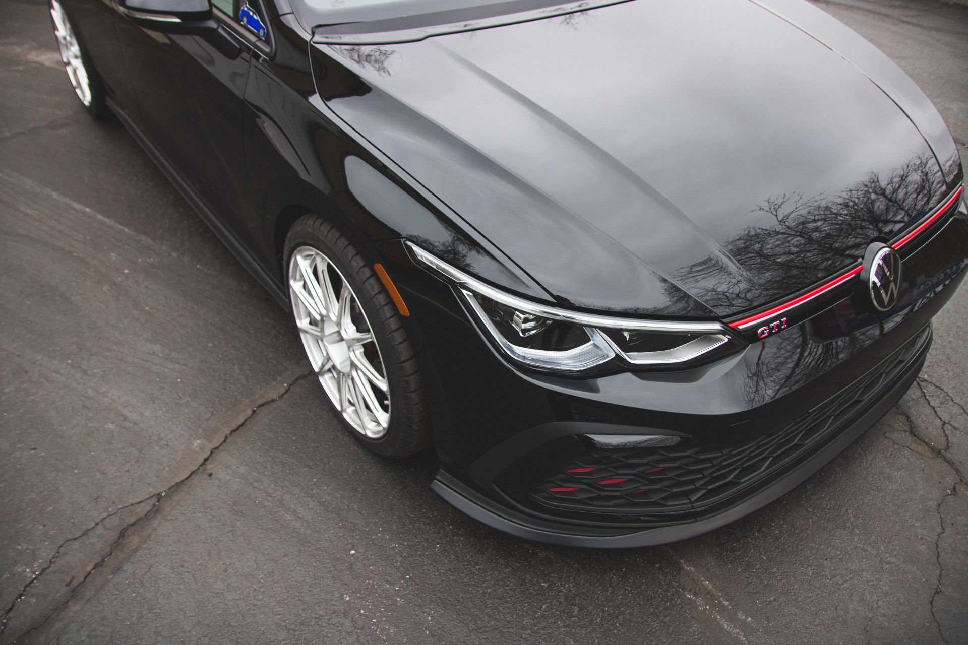 Black sedan parked on wet pavement, front-left view with glossy hood and chrome wheels