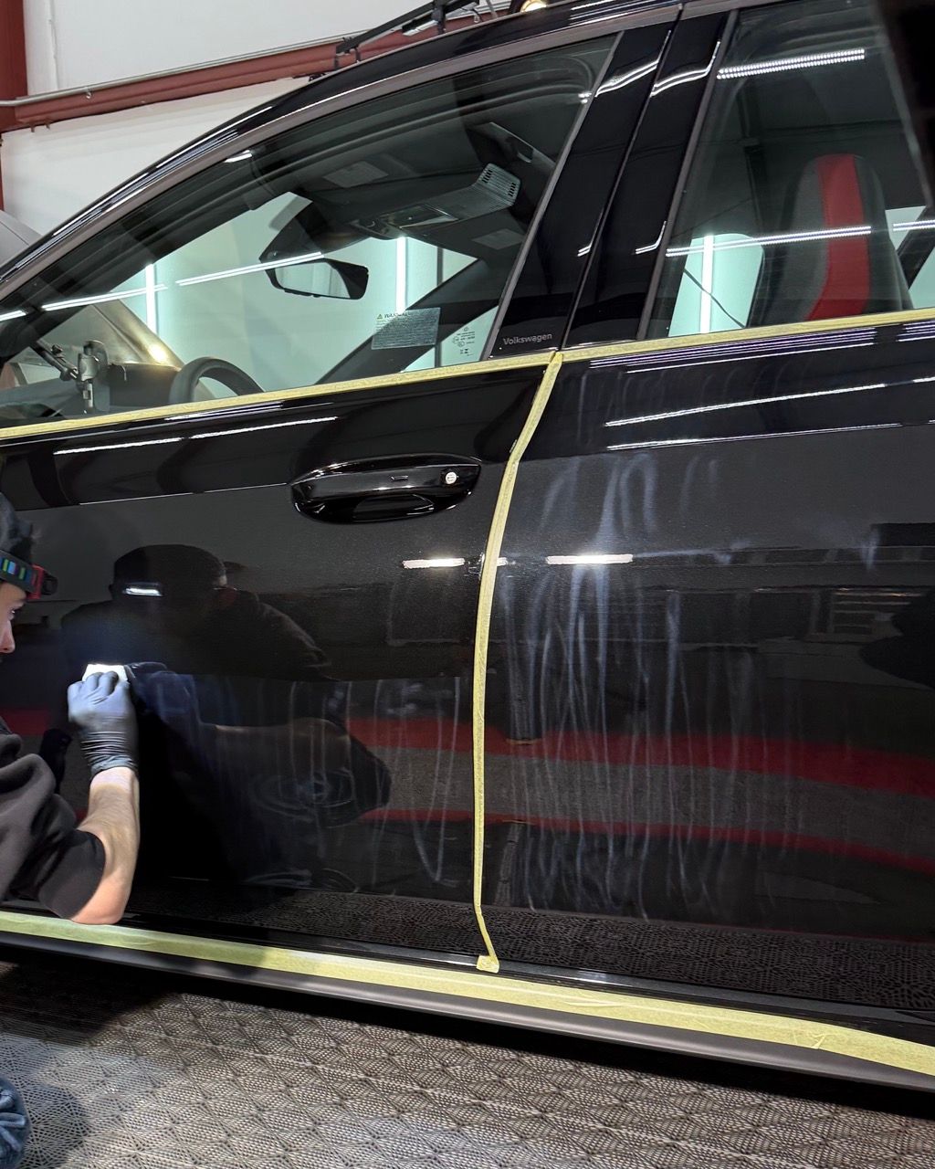 Black car door being polished, with masking tape along the trim in a garage.