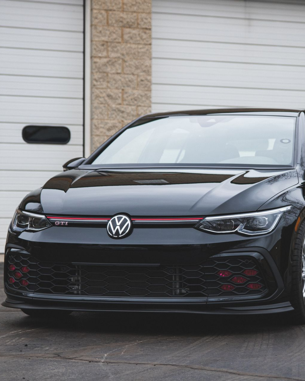 Black Volkswagen hatchback parked in front of a garage door with a red accent stripe on the grille